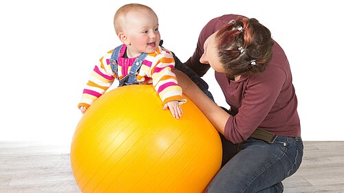 A lady holding a baby on an exercise ball.